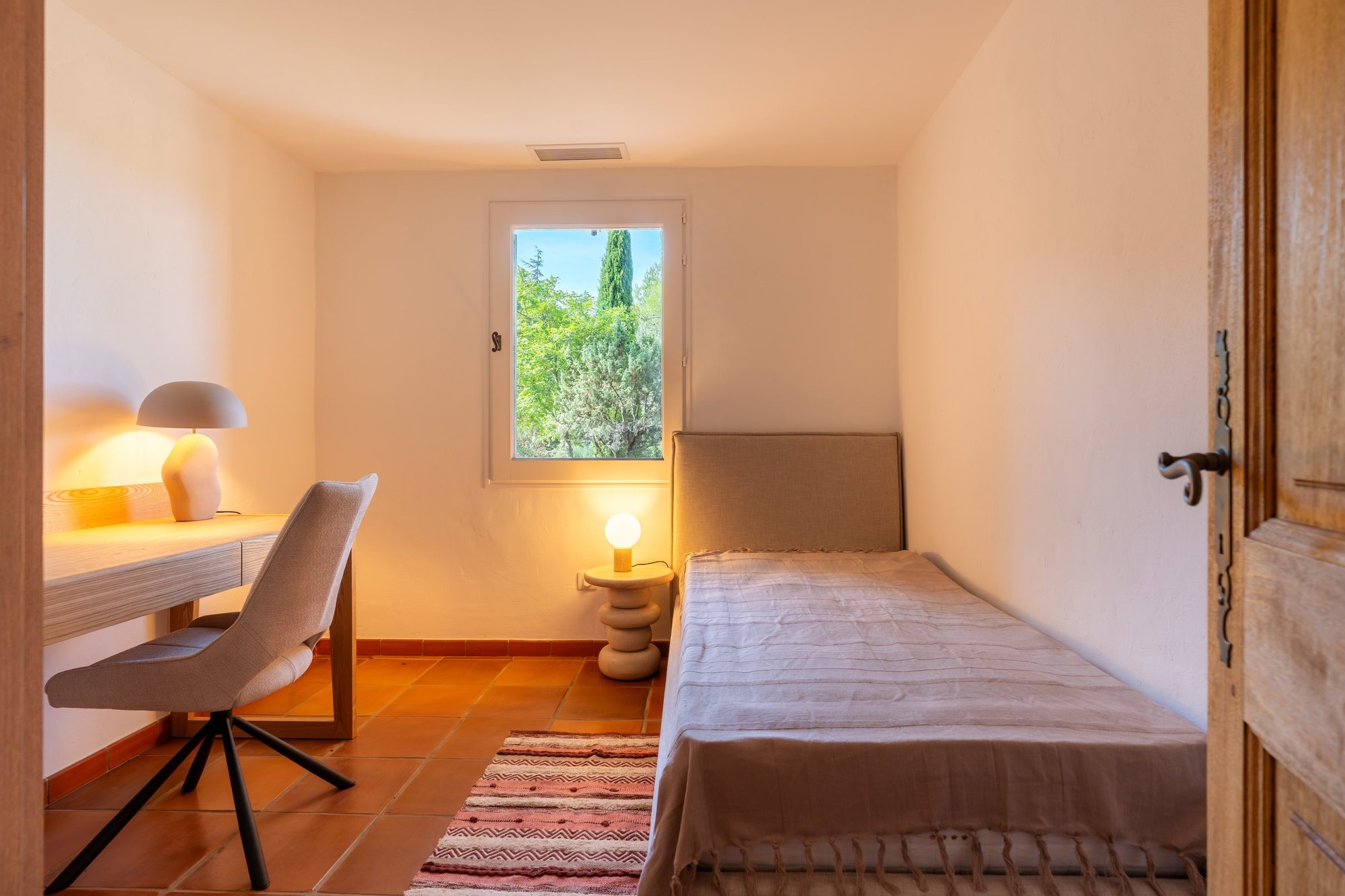 Chambre d'appoint avec lit simple, bureau et tapis kilim.