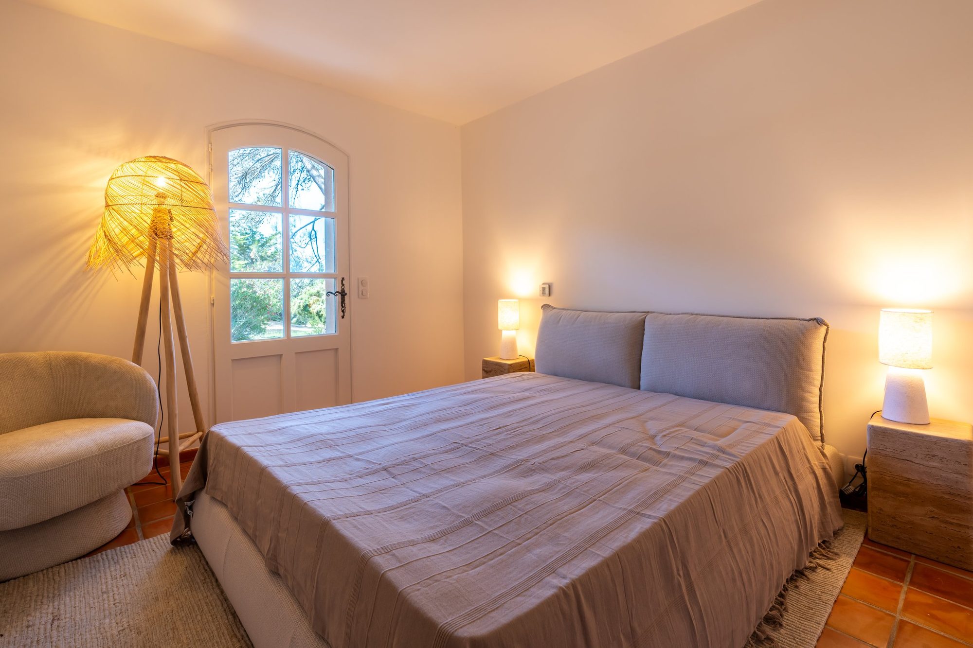 Chambre à la tête de lit capitonnée, lampes de chevet et fauteuil bouclé.