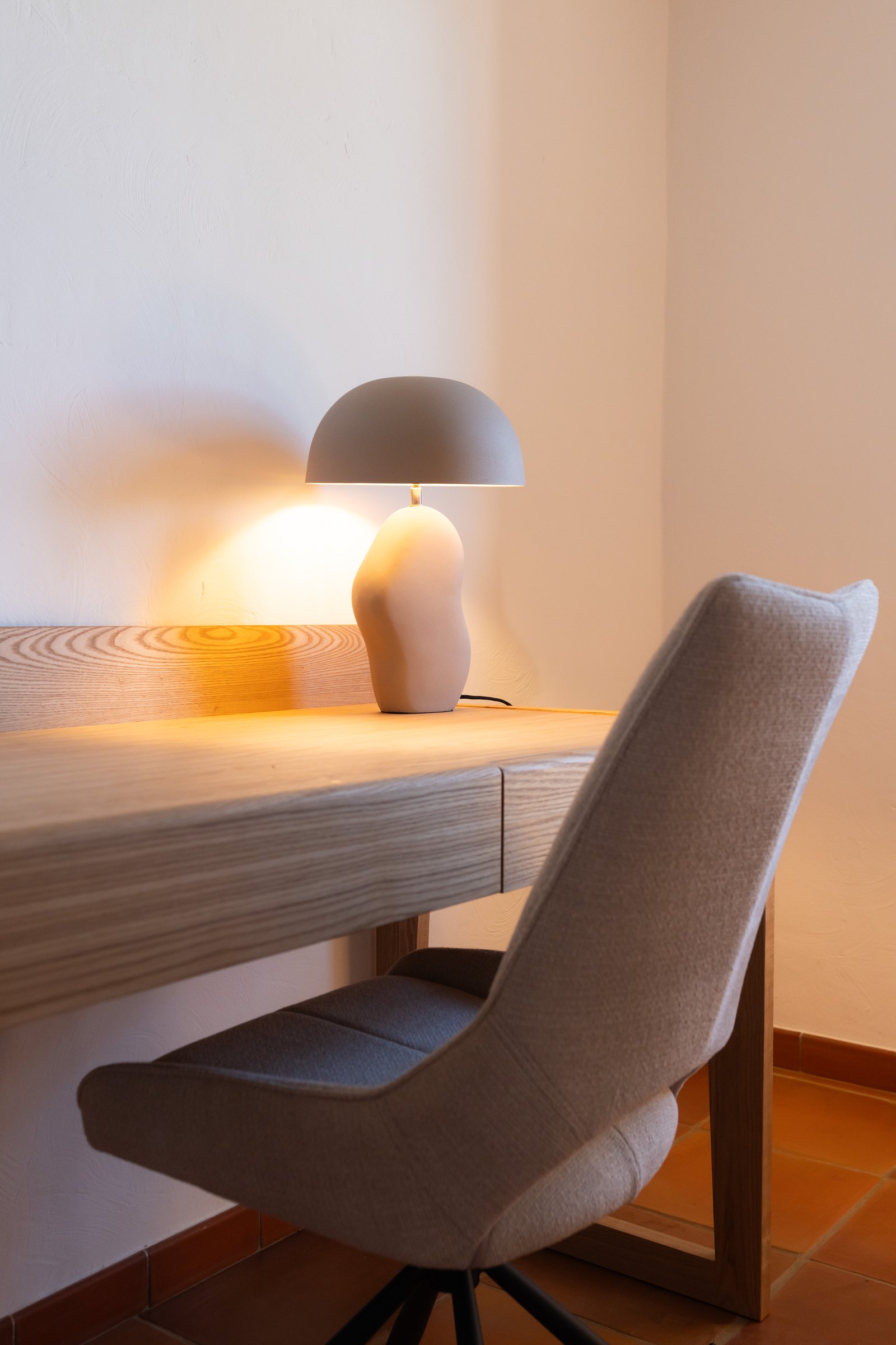 Bureau en bois clair et chaise pivotante grise devant un mur nu.