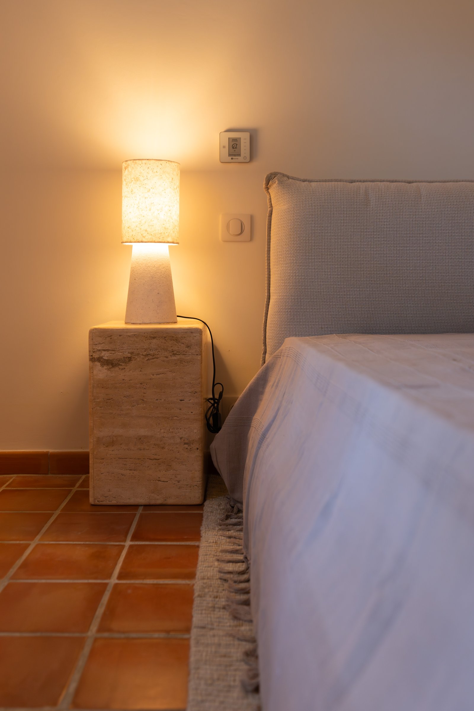 Table de chevet en bois brut et lampe à abat-jour clair.