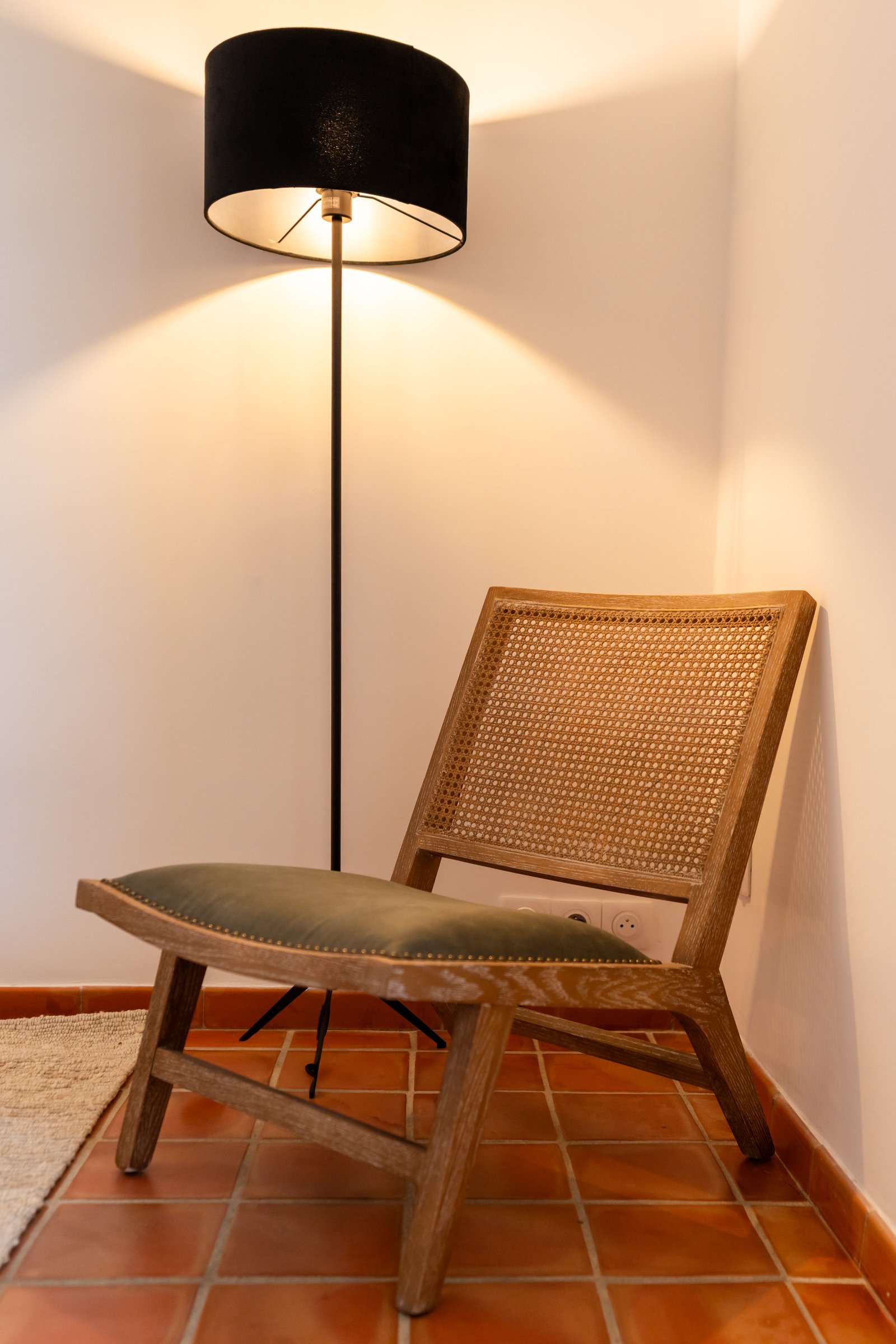 Fauteuil bas en bois et cannage sous un lampadaire à abat-jour noir.