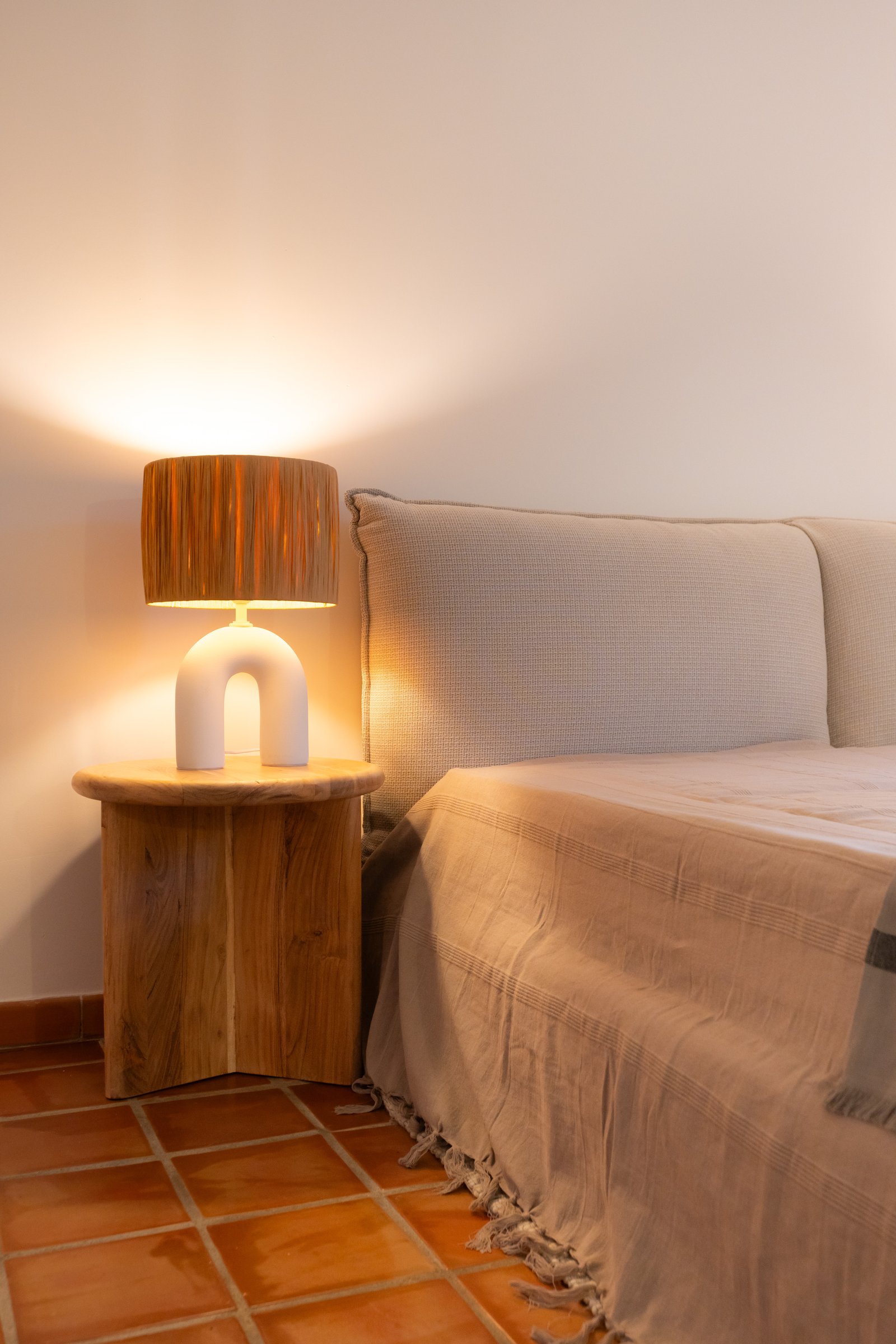 Chevet arrondi en bois et lampe sculpturale près du lit.