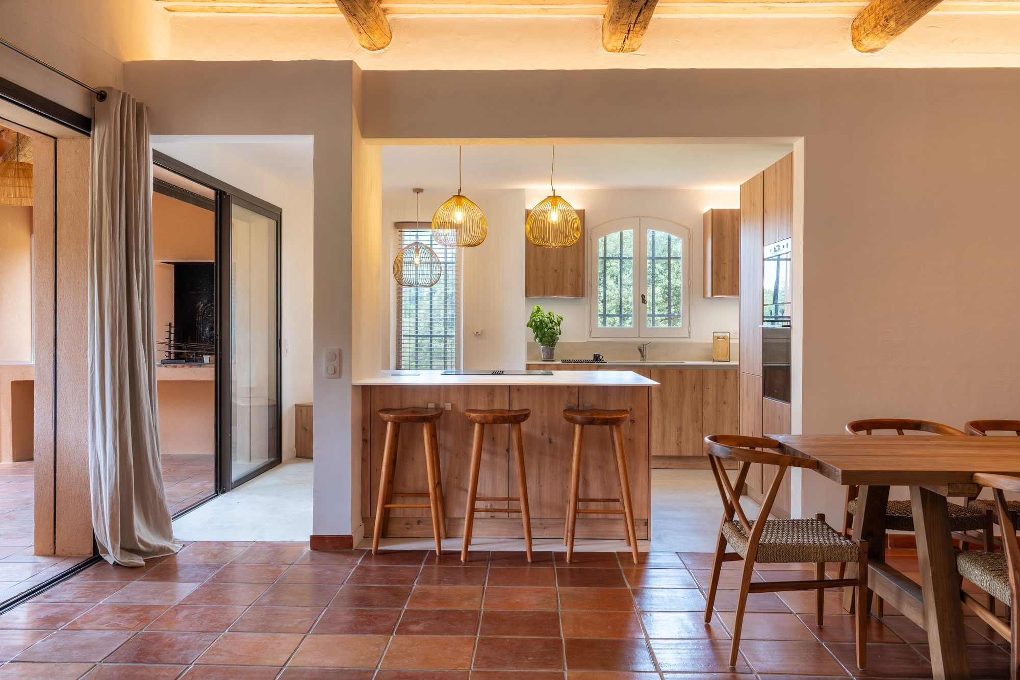 Cuisine ouverte en bois clair avec îlot, tabourets de bar et suspensions en verre ambré.