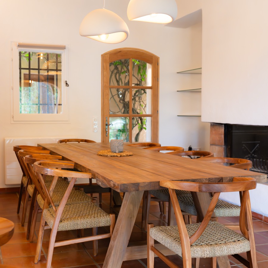 Grande table en bois massif entourée de chaises tressées sous une charpente apparente.