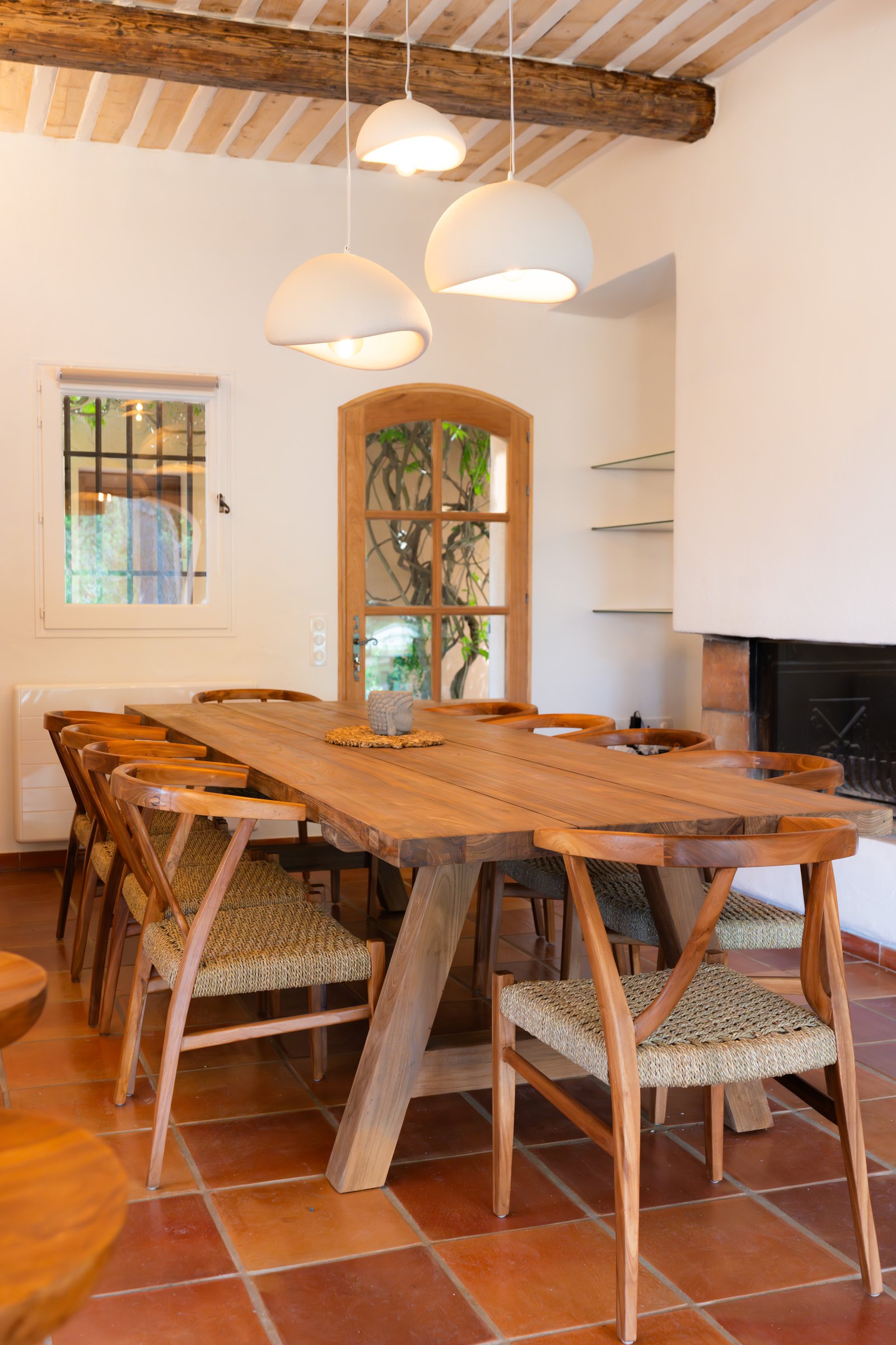 Grande table en bois massif entourée de chaises tressées, sous une charpente provençale apparente.