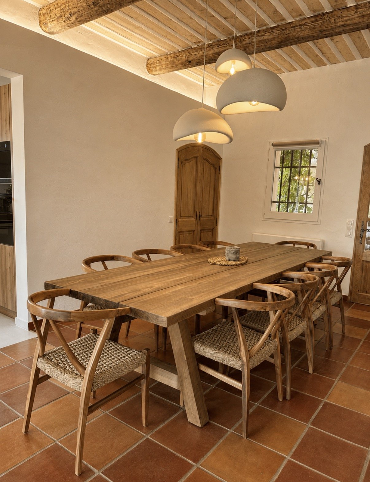 La même pièce meublée d'une grande table en bois clair et de chaises tressées.